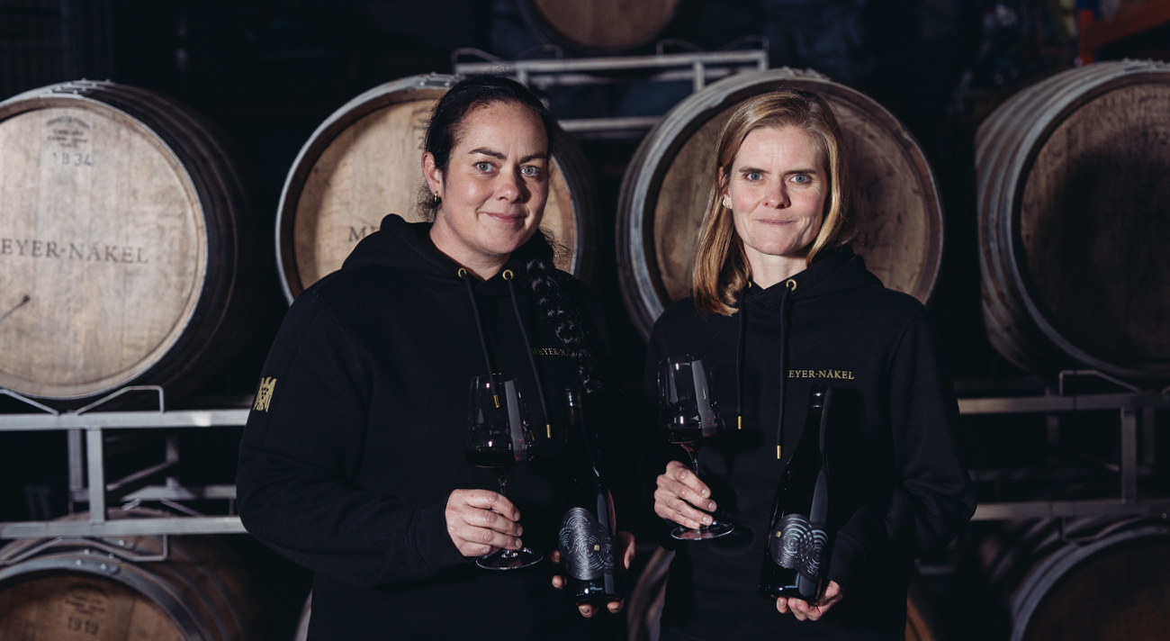Weingut Meyer-Näkel – Lost Barrels Die Winzerschwestern Heike und Dörte Näkel halten Weingläser vor Holzfässern.